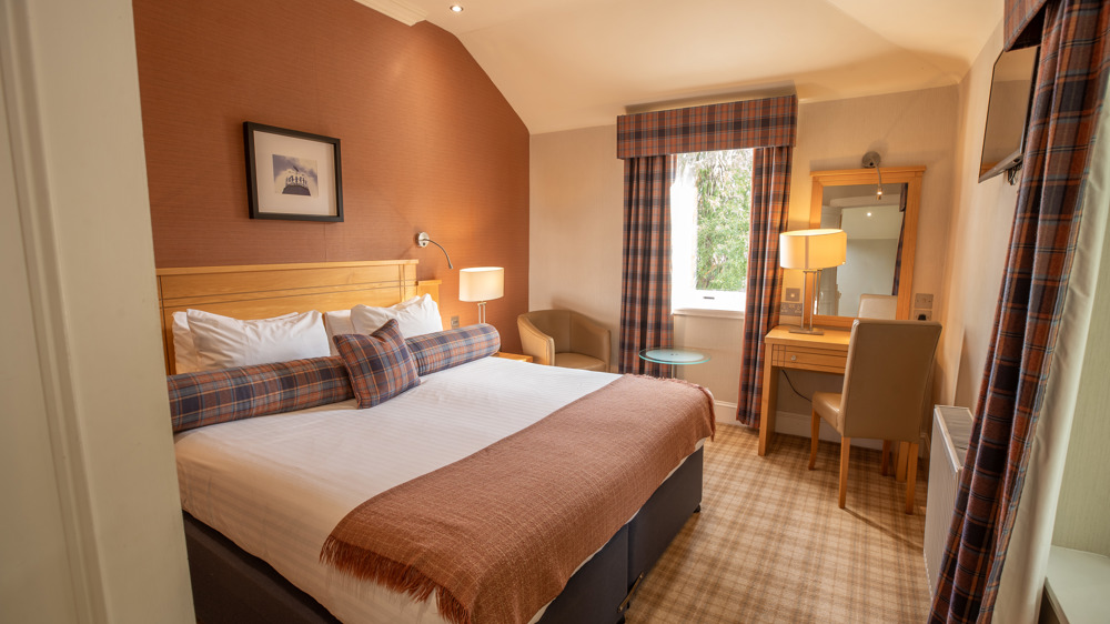 Studio apartment bedroom with king-sized bed, vanity & chair, and windows.