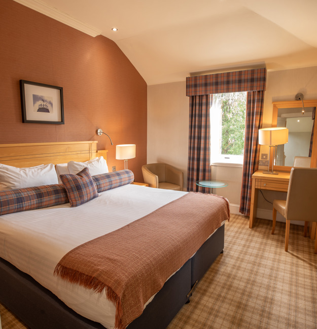 Studio apartment bedroom with king-sized bed, vanity & chair, and windows.