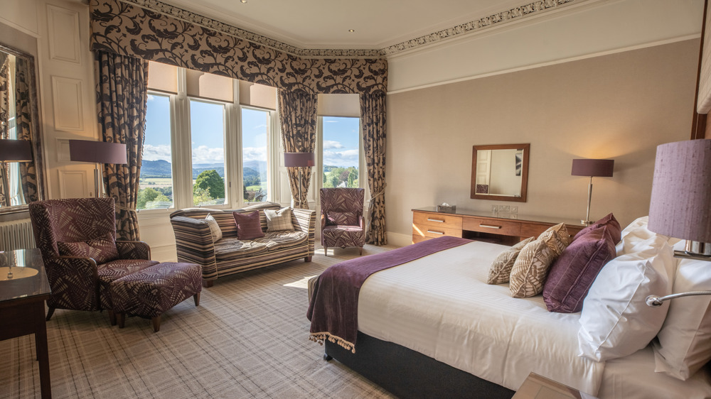 Leigh signature double with king-sized bed facing a window with two chairs and a loveseat in front of the window.