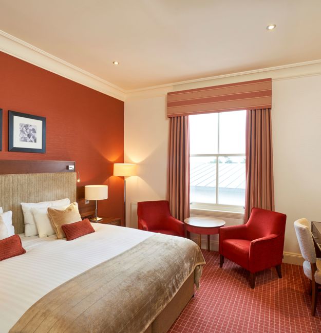 Feature double bedroom with king-sized bed, bedside table, two chairs in front of a window.