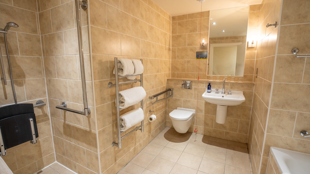 Accessible bathroom with toilet, sink, mirror, towel rack, bathtub, separate walk-in shower with shower chair.