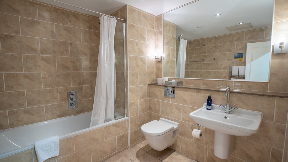 Bathroom with shower over tub, toilet, sink and mirror.