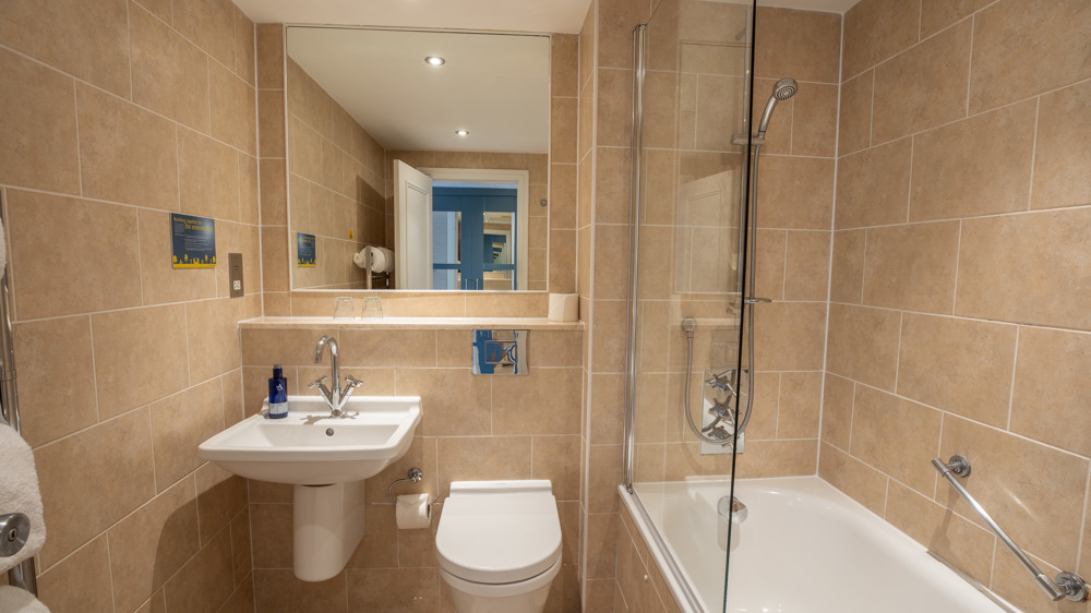 Bathroom with sink, mirror, toilet, and shower over bath.