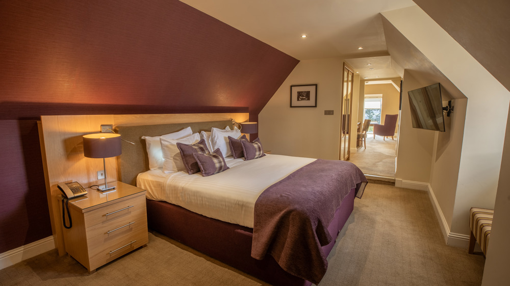 Signature suite bedroom with king-sized bed and bedside tables. The rest of the suite is visible through the door.