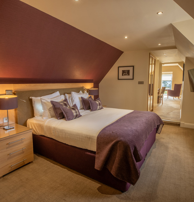 Signature suite bedroom with king-sized bed and bedside tables. The rest of the suite is visible through the door.