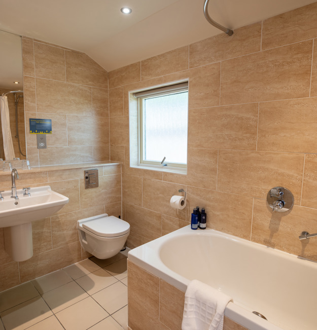 Bathroom in studio apartment with sink, toilet, mirror, shower over bath, and towel rack