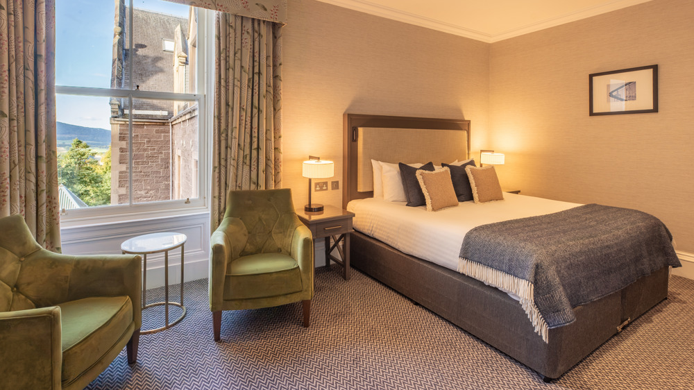 Feature double bedroom with two chairs in front of a window and a king-sized bed.