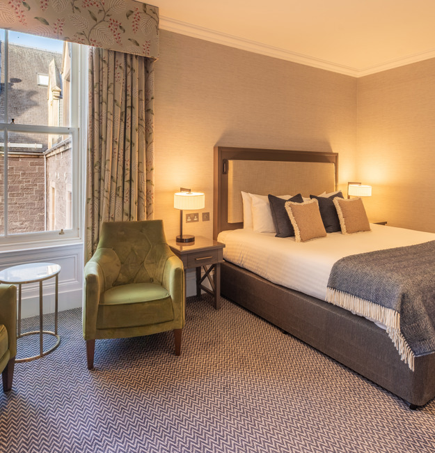 Feature double bedroom with two chairs in front of a window and a king-sized bed.