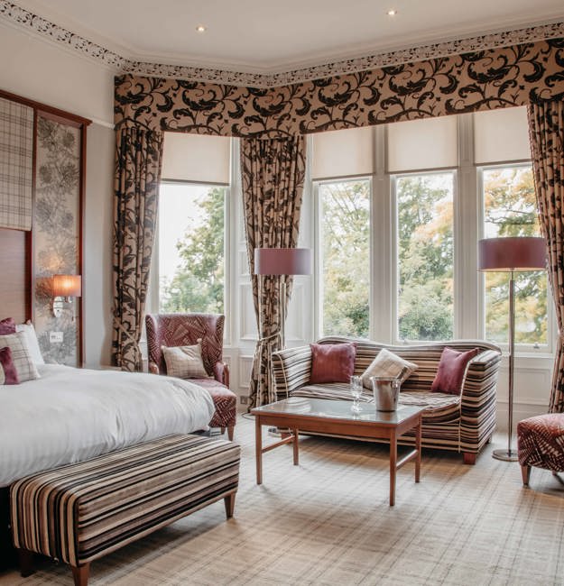 Leigh signature double with king-sized bed, two chairs and a loveseat in front of a bay window.