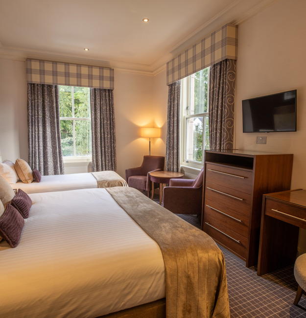 Room for 3 with a king-sized bed, a single bed, a vanity wit chair, dresser, TV on the wall, two chairs and two windows.